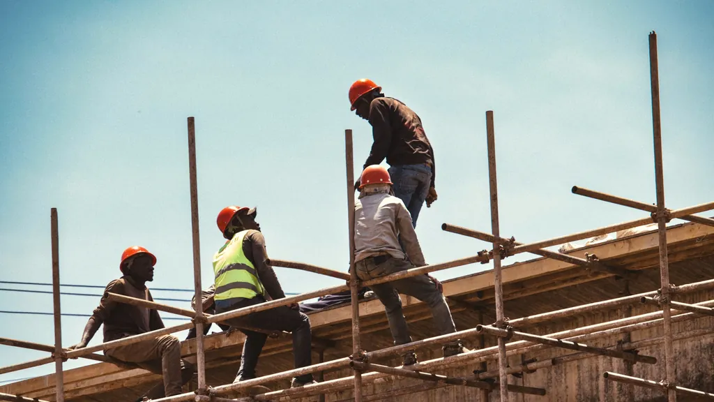 Trabalhadores com capacete sobre andaimes numa obra, contra céu limpo