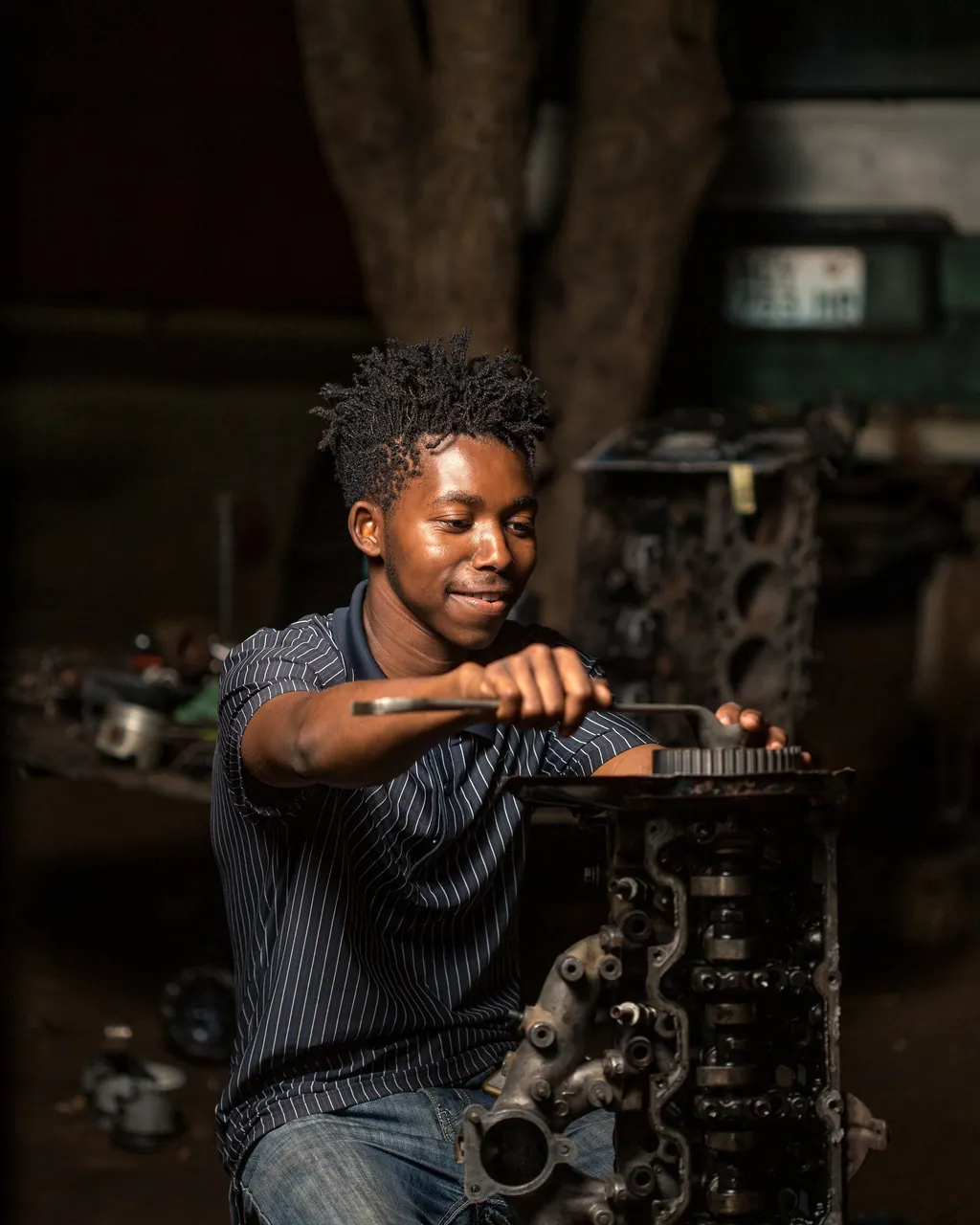 Jovem mecânico sorri enquanto repara um bloco de motor numa oficina em Maputo