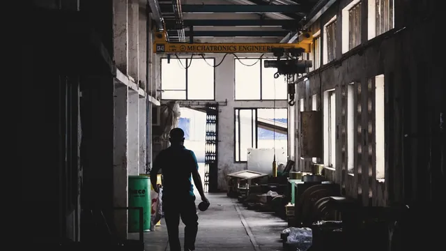 Pessoa a caminhar num corredor de uma nave fabril, em contraluz
